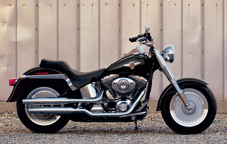 a black and silver motorcycle parked in front of a wooden building with a metal fence behind it