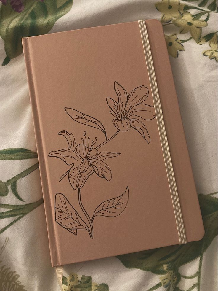 a notebook with flowers drawn on it sitting on top of a floral print sheet covered bed