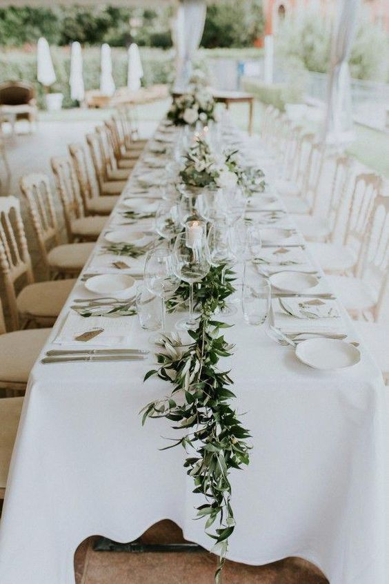 the long table is set with white linens and greenery