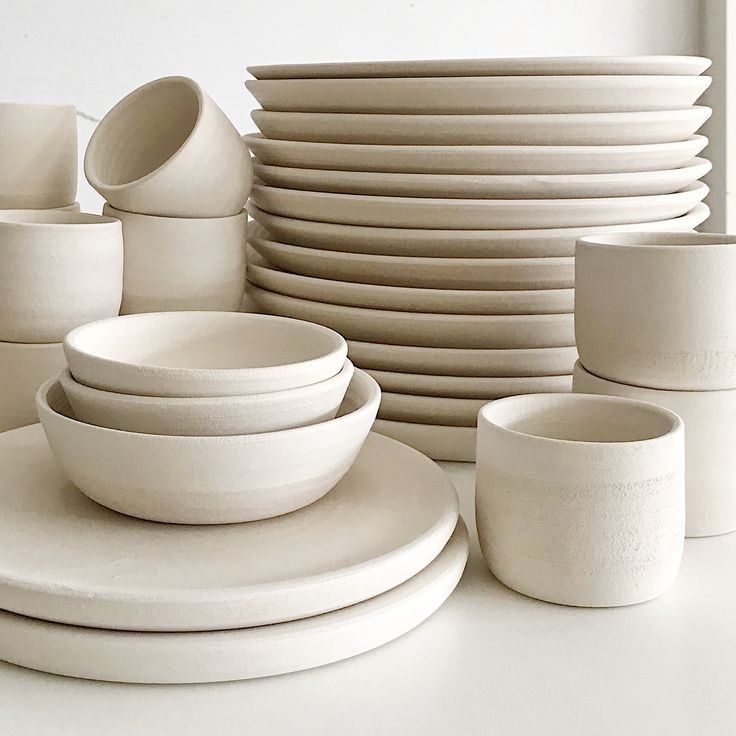 a stack of white plates and cups sitting on top of a table next to each other