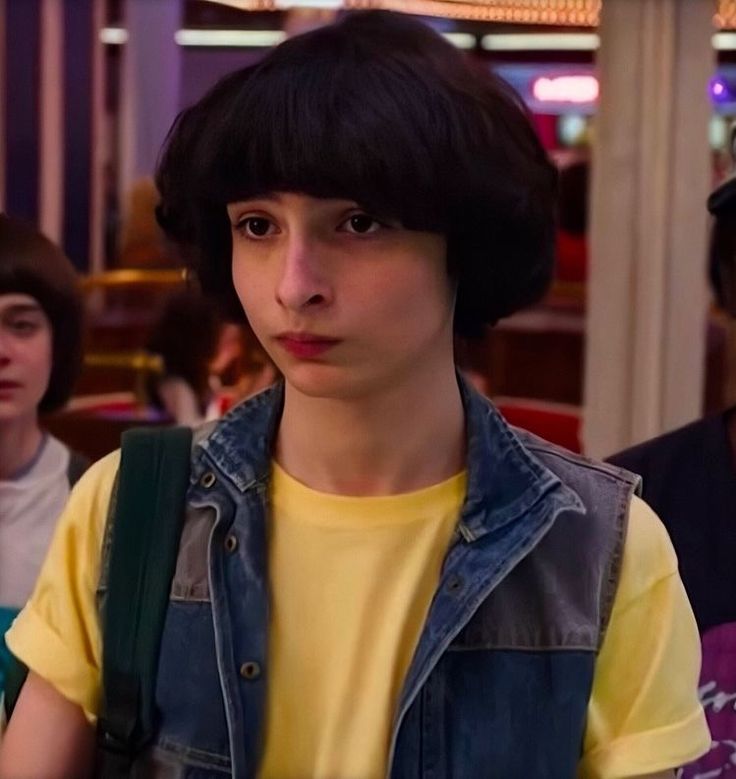 a young boy in a yellow shirt and jean vest standing next to two other people