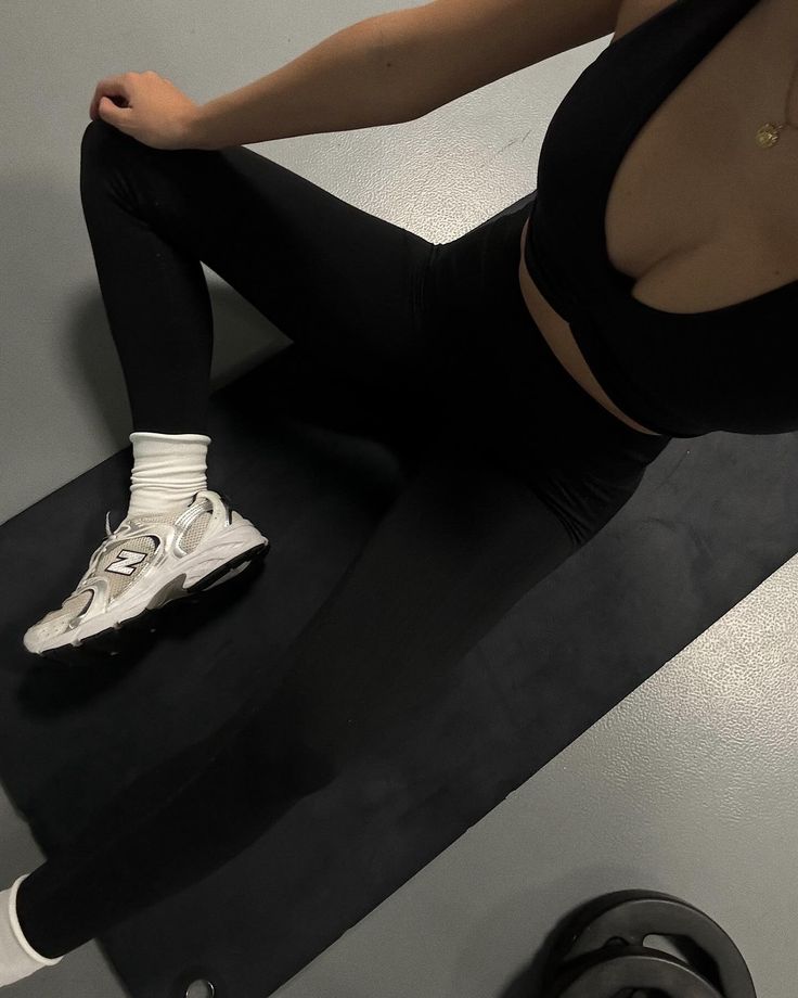 a woman sitting on top of a black mat with her feet propped up in the air