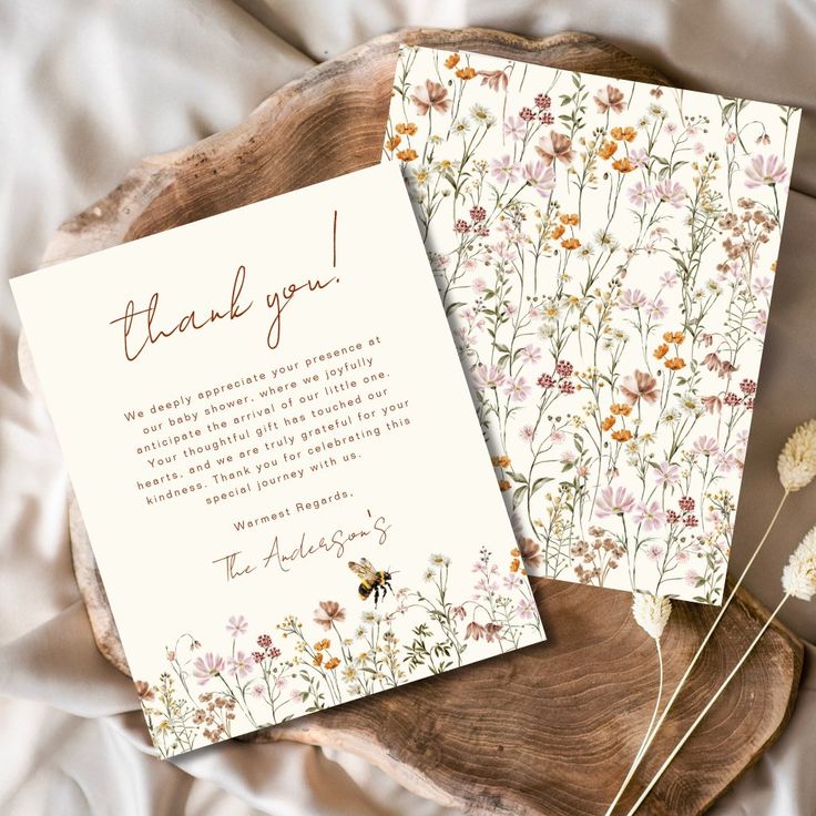 two cards with flowers on them sitting on top of a wooden plate next to each other