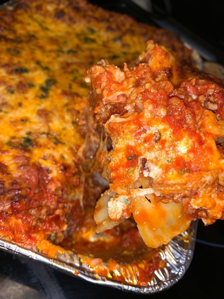 a piece of lasagna being lifted from a casserole dish with meat and cheese