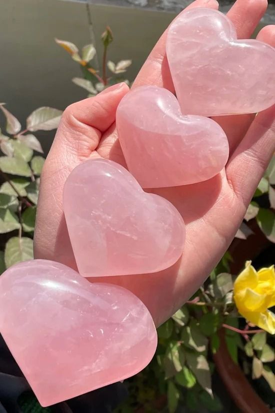 three pink heart shaped stones held in someone's hand next to some yellow flowers