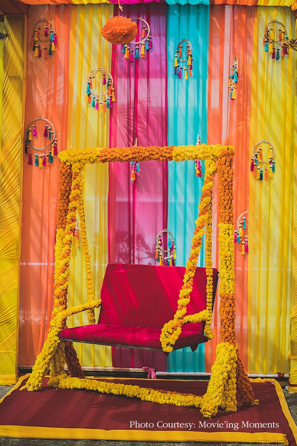 a red chair sitting in front of a colorful backdrop with flowers on the floor and curtains behind it