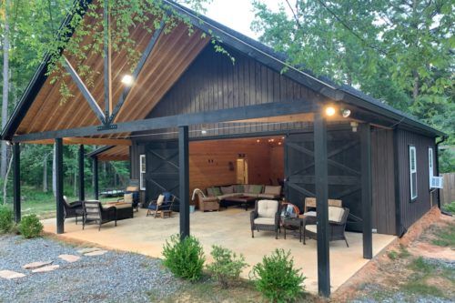 a covered patio area with chairs and tables in front of a barn style building surrounded by trees