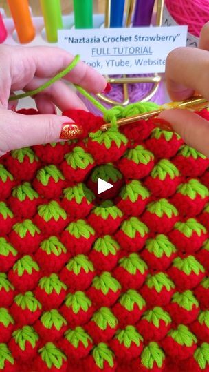 two hands are working on a crocheted red and green object with yarn in the background