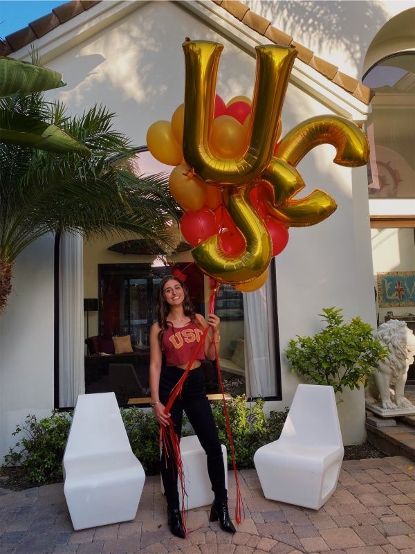 a woman standing in front of a house holding up a large balloon shaped like the letter u