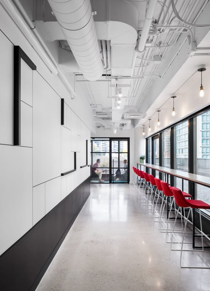 an empty office with red chairs and black accents on the walls, along with large windows