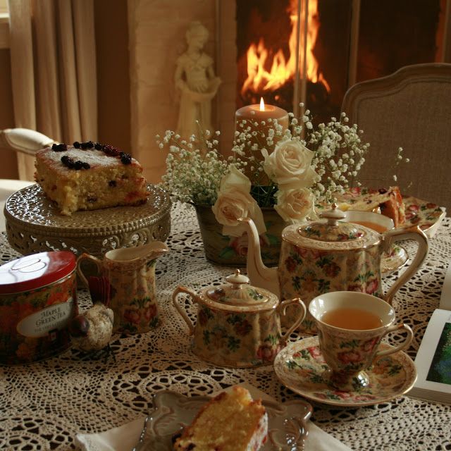 a table topped with tea cups and cake next to a fire place filled with flowers