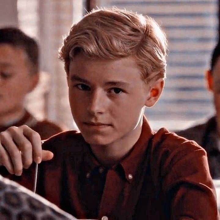 a young boy sitting in front of a computer screen with his hand on the keyboard