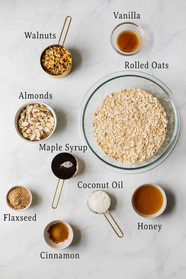 ingredients to make oatmeal cookies laid out on a white counter top, including almonds, maple syrup, coconut oil, cinnamon and vanilla