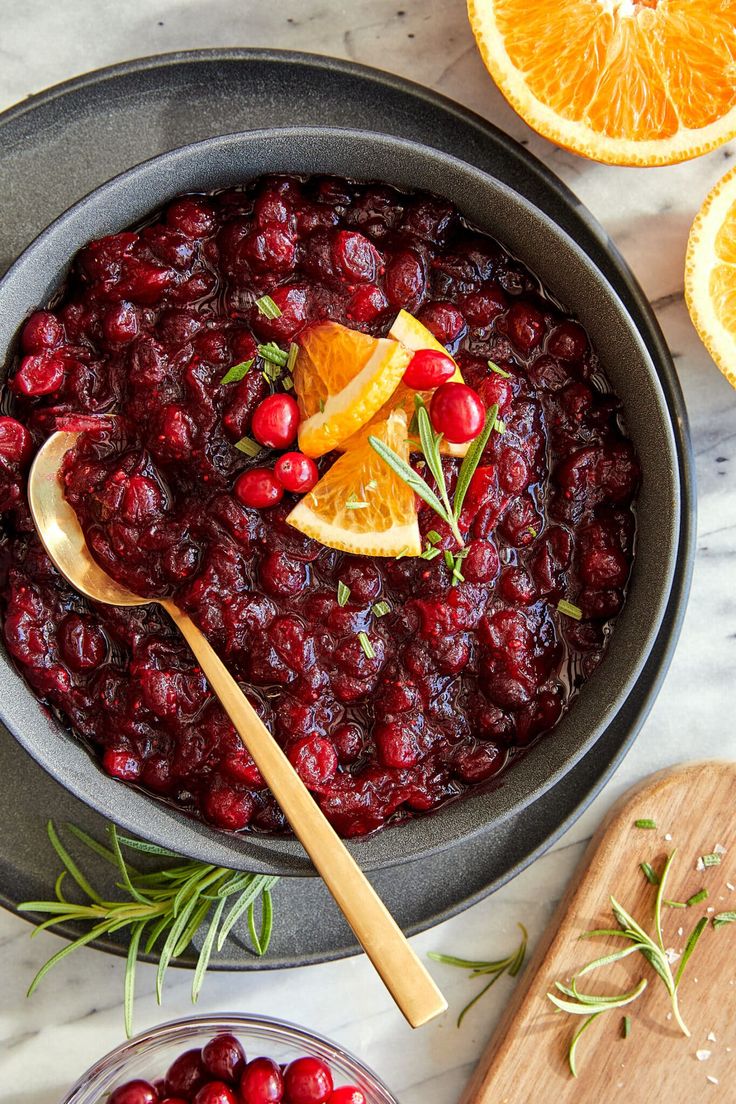 cranberry sauce in a bowl with orange slices and rosemary garnish on the side