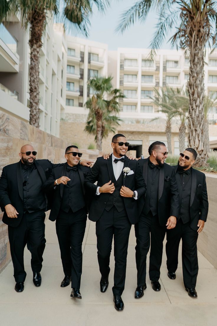 a group of men in tuxedos walking down a sidewalk next to palm trees