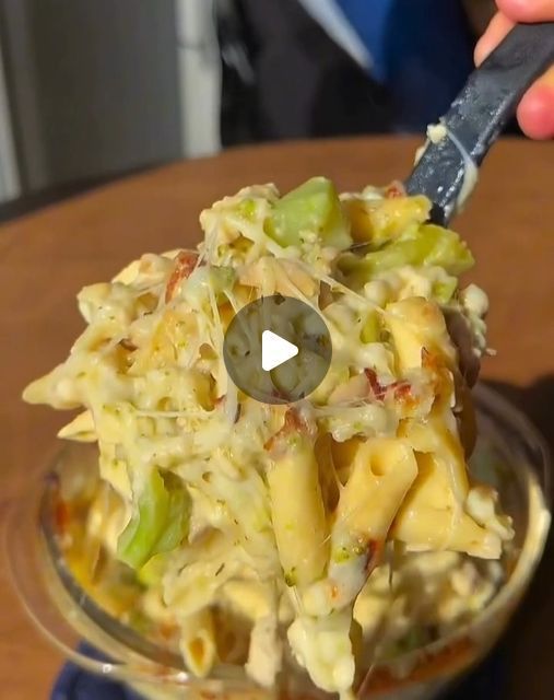 a person holding a knife over a bowl filled with macaroni and cheese salad