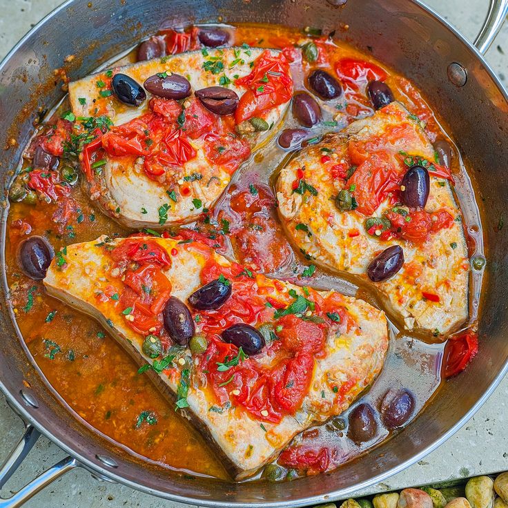 some food is cooking in a pan with olives and tomatoes on top, along with other foods