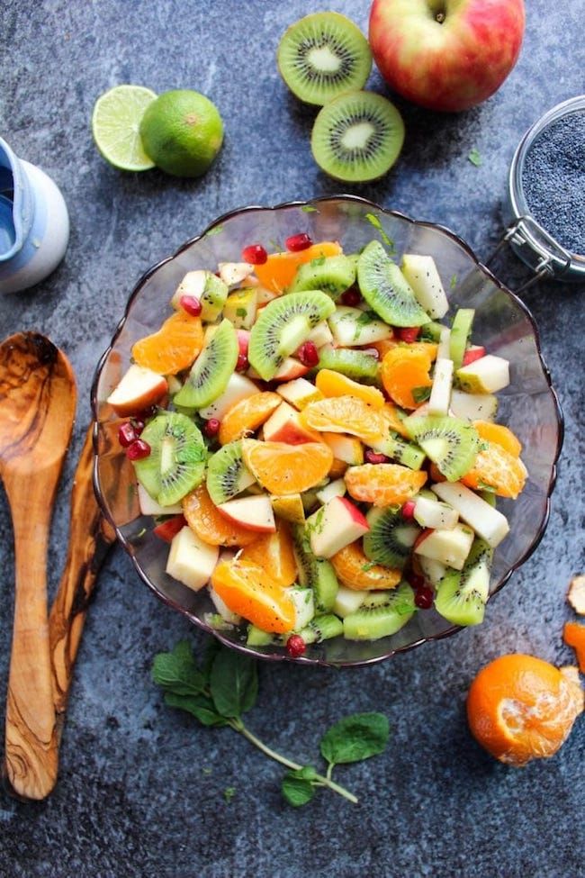 a glass bowl filled with fruit next to sliced oranges and kiwi