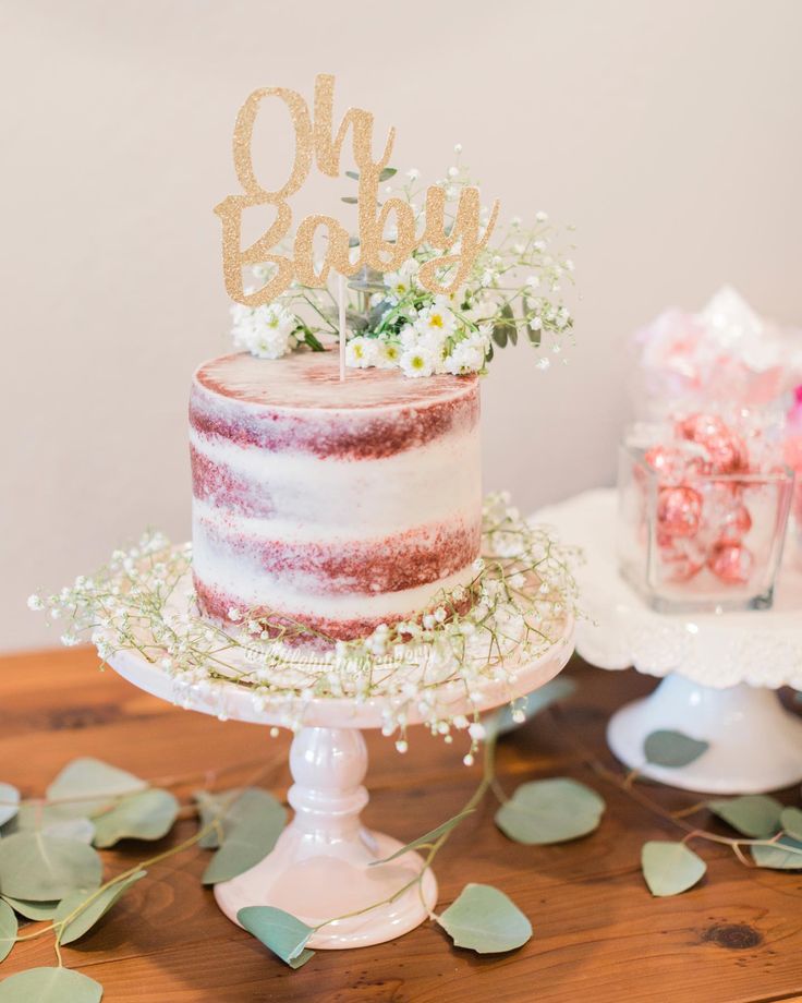 a pink and white cake sitting on top of a wooden table next to greenery