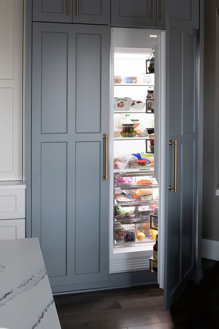 an open refrigerator door in a kitchen with blue cabinets and white counter tops, along with wooden flooring