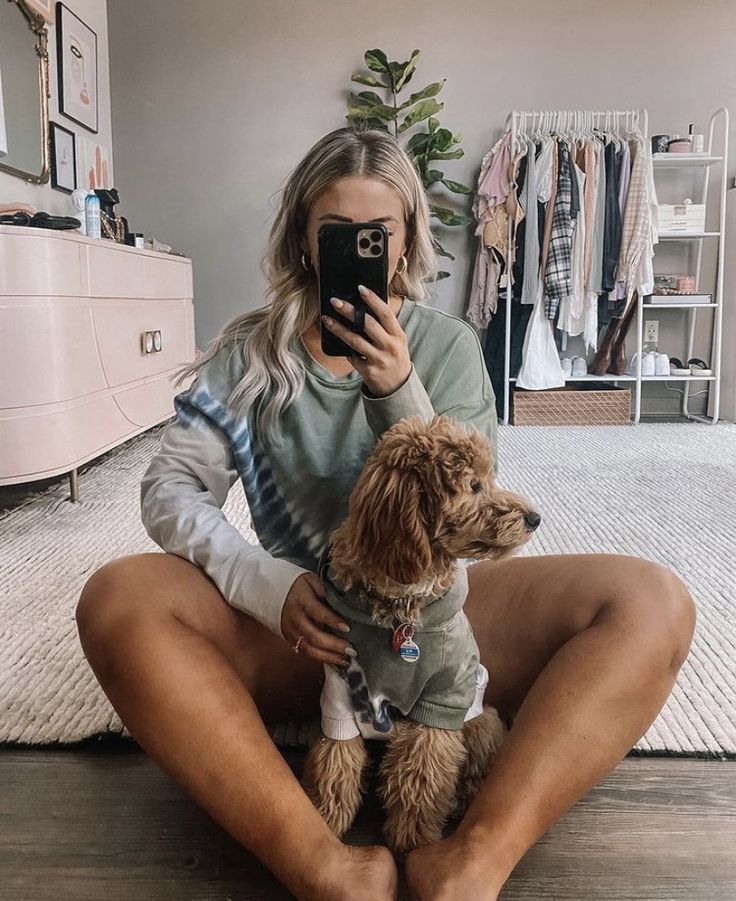 a woman sitting on the floor holding a dog and taking a selfie with her phone