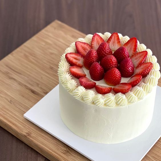 a cake with strawberries on top sitting on a cutting board next to a knife