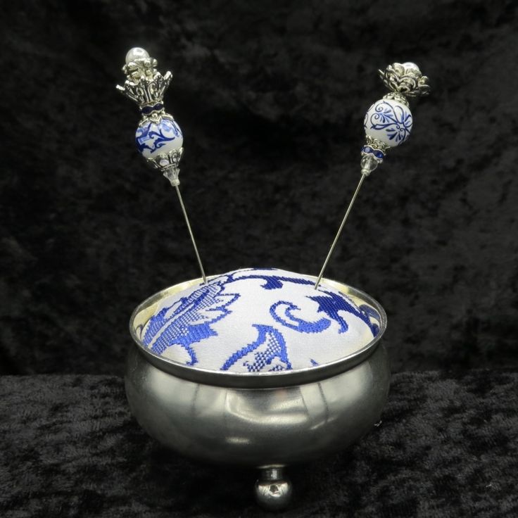 a silver bowl with blue and white designs on the inside is holding three metal balls