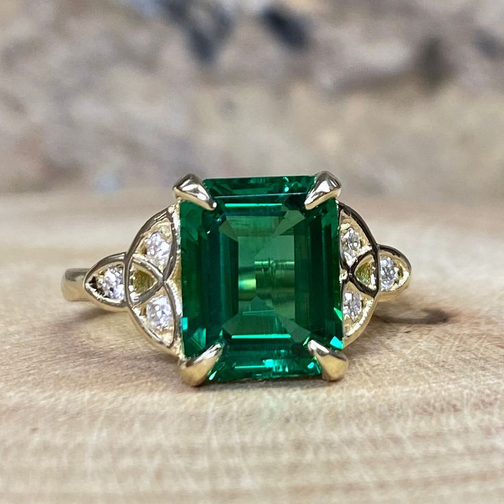 an emerald and diamond ring sitting on top of a piece of wood