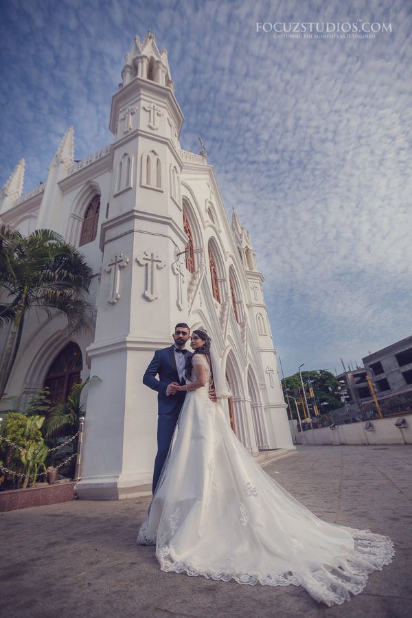 a bride and groom standing in front of a white church with palm trees around them