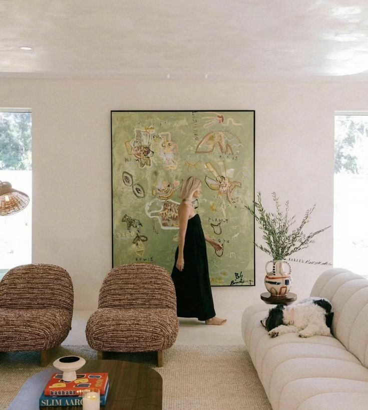 a woman walking through a living room with two couches and a painting on the wall