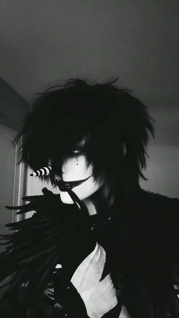 a man with black hair and wings on his face is posing for a photo in a dark room