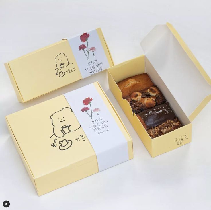 three boxes filled with different types of pastries on top of a white tablecloth