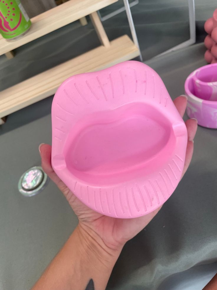 a person holding a pink heart shaped bowl on top of a gray table next to other bowls