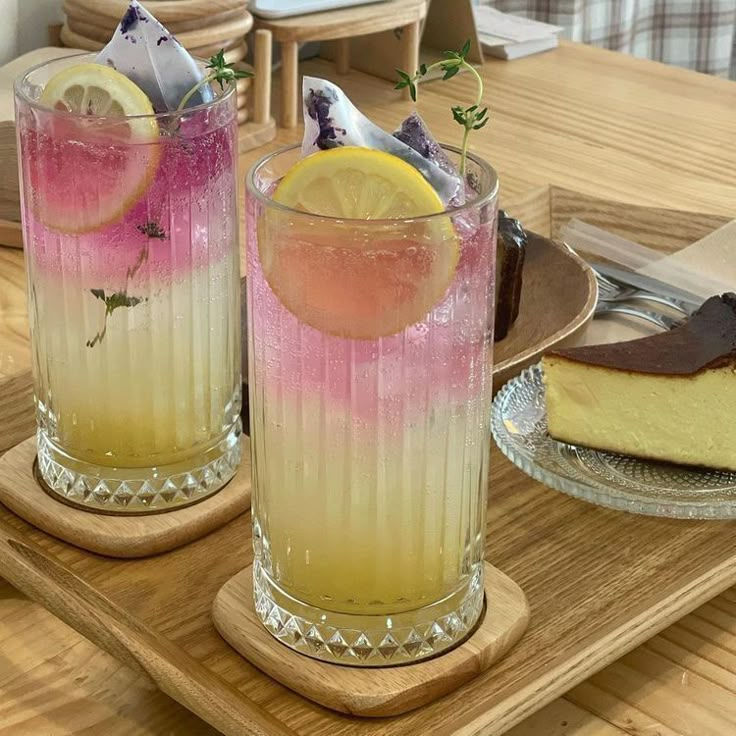 two glasses filled with different colored drinks sitting on top of a wooden tray next to each other