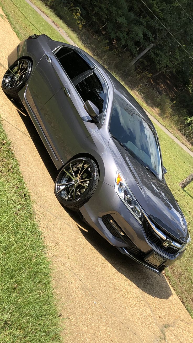 a silver car parked on the side of a dirt road next to a lush green field