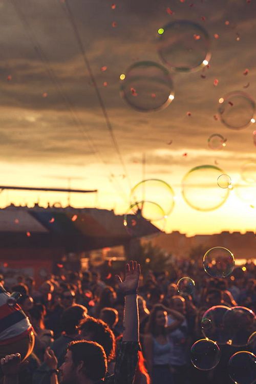 many people are blowing soap bubbles in the air at sunset or dawn, with one person holding up his hand