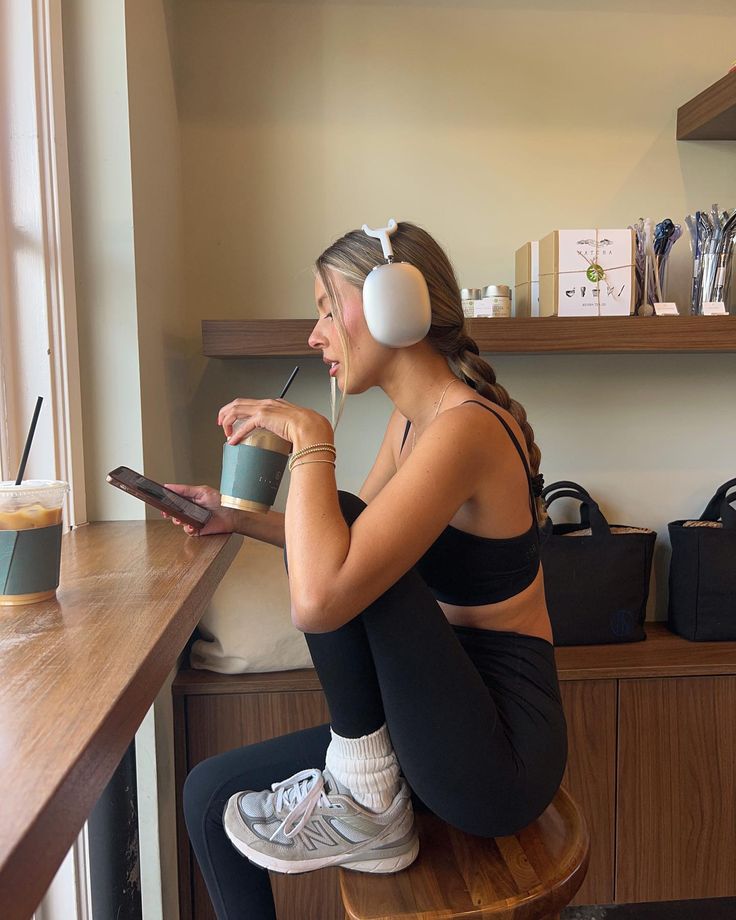 a woman sitting at a table with headphones on drinking from a cup and listening to music