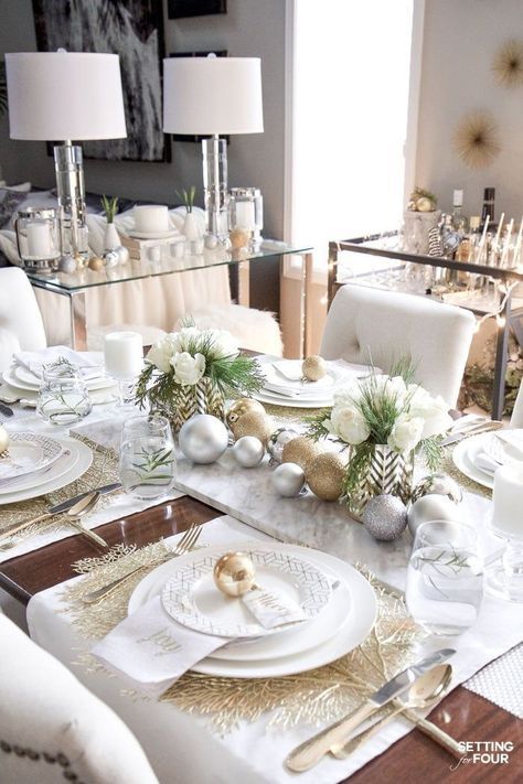 a dining room table set for christmas with white and gold decorations on the place settings