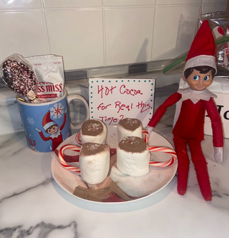 an elf is sitting on the counter next to some marshmallows and candy canes