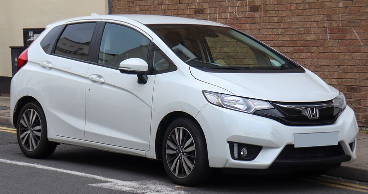 a white honda jazz parked on the side of the road next to a brick building