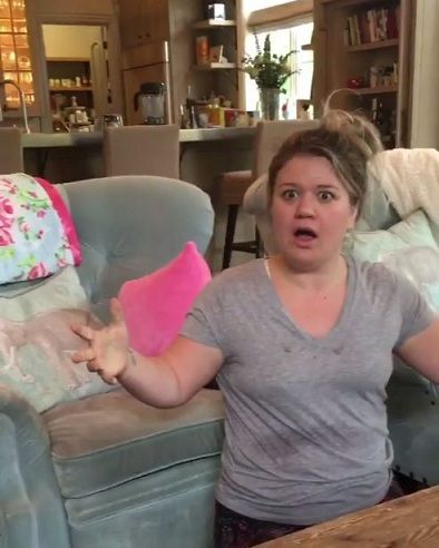 a woman sitting on a couch holding a pink pillow in her hand and looking surprised at the camera