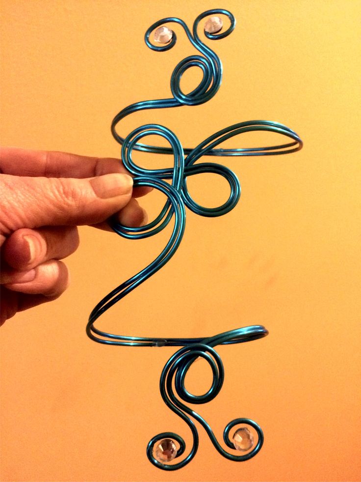 a hand holding a wire sculpture on top of a yellow wall with an orange background