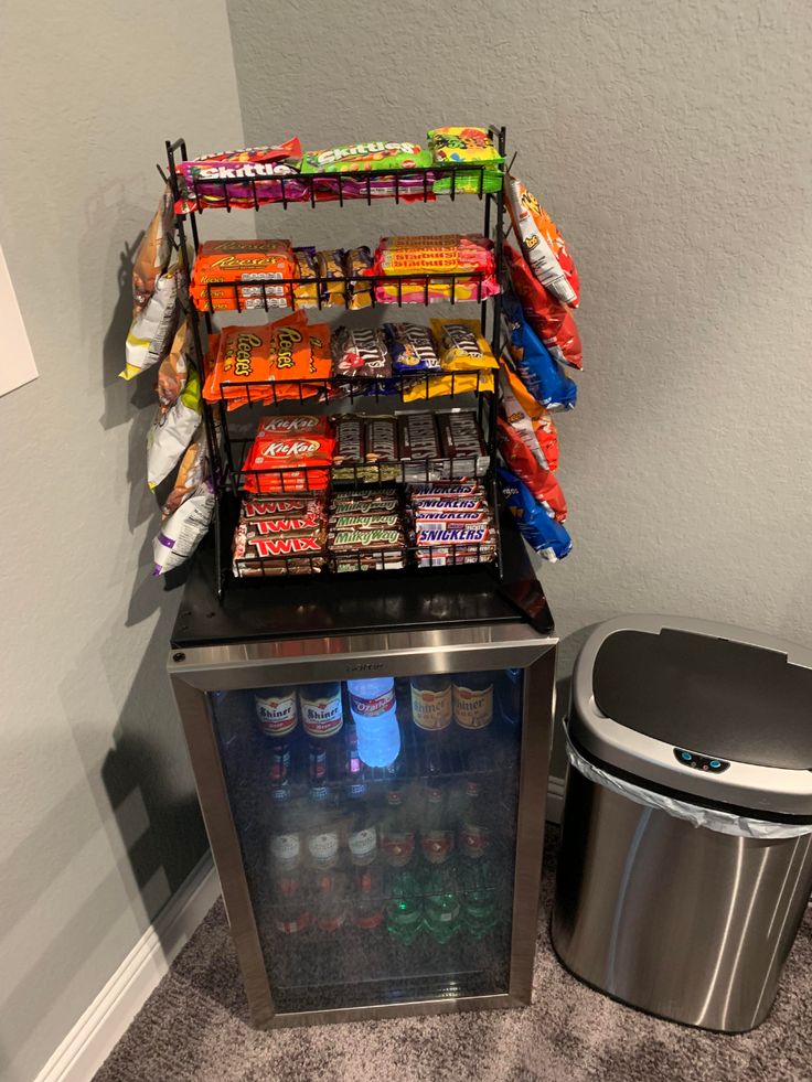 a cooler with snacks and drinks on it next to a trash can in the corner