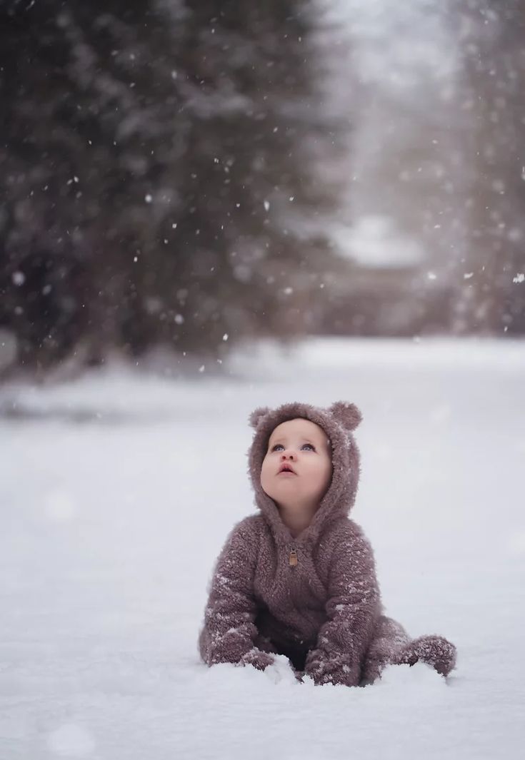 a baby in a bear suit laying in the snow with his head up and eyes closed