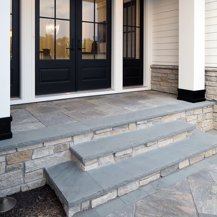 two black doors are on the side of a house with steps leading up to it