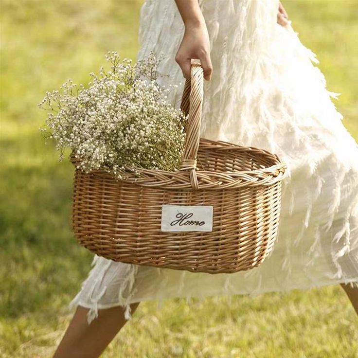 a woman in white dress carrying a wicker basket with baby's breath flowers