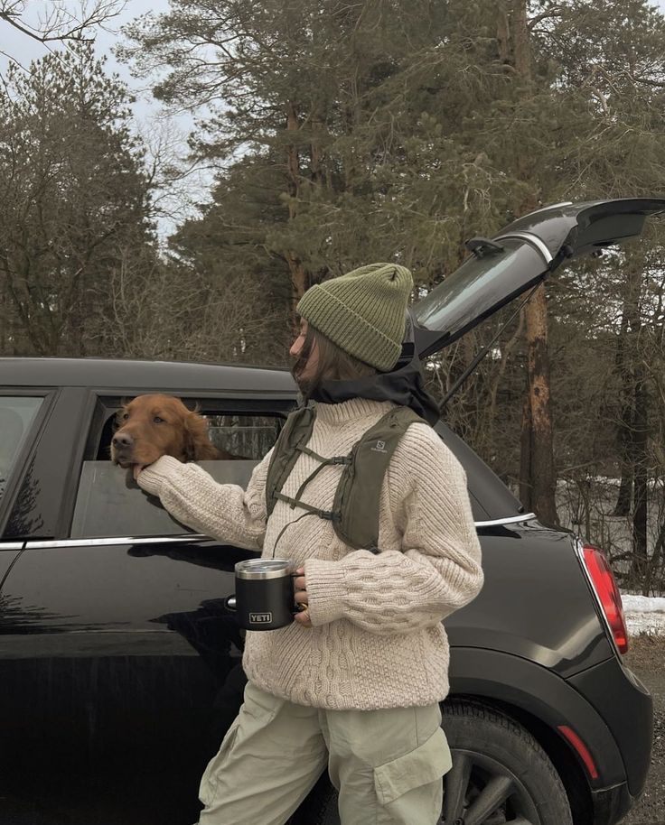 a man holding a dog in his hand while standing next to a car