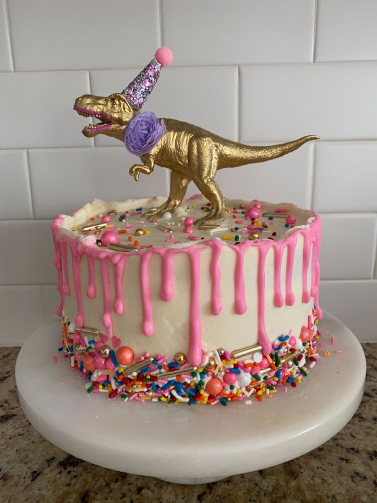 a birthday cake decorated with sprinkles and a gold dinosaur figure on top