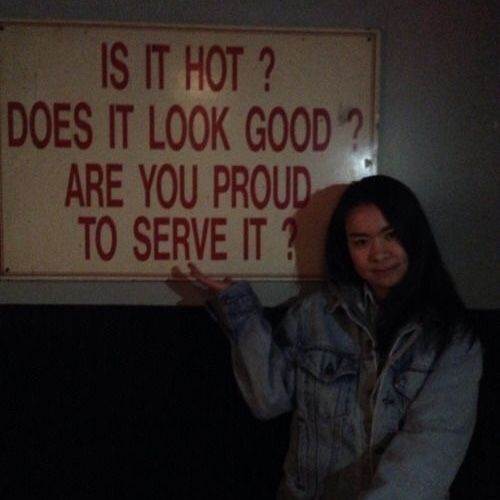 a woman standing in front of a sign that says is it hot? does it look good are you proud to serve it?