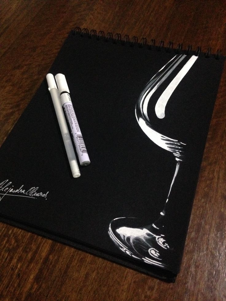 a black notebook with white writing on it and a wine glass next to the pen